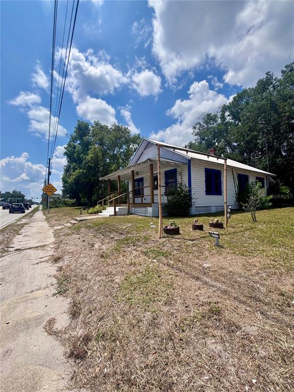 A white single-story house with blue trim and a front porch sits beside a road — 490 N SPRING GARDEN AVENUE, DELAND, FL