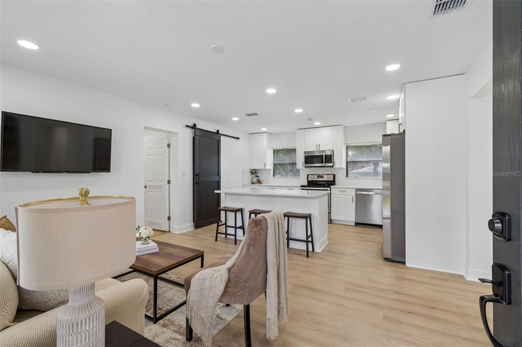 An open-concept kitchen and living area featuring white cabinets, a kitchen island, and wood flooring — 1702 W JOHNSTON AVENUE, TAMPA, FL