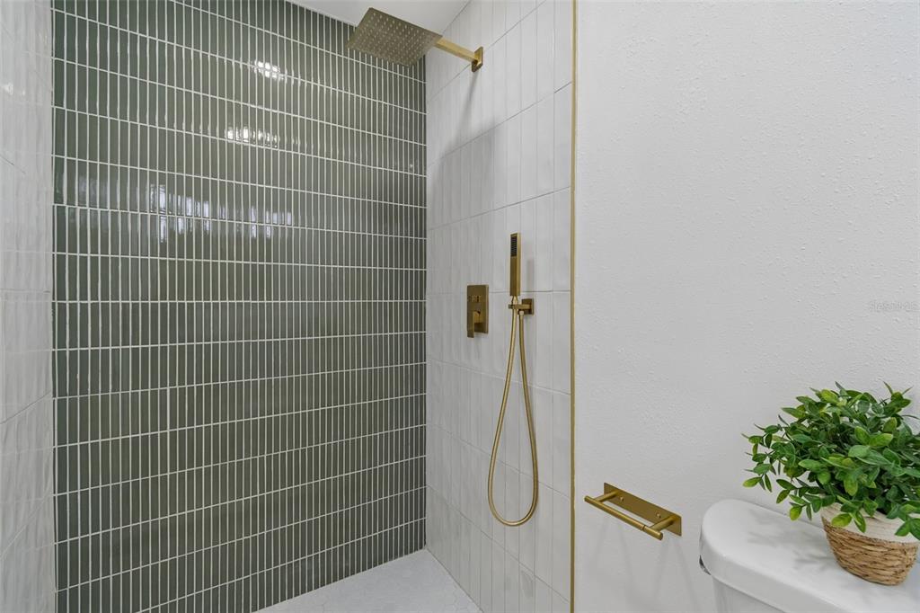 A bathroom shower features olive green vertical tiles, white wall tiles, and gold-toned fixtures — 1702 W JOHNSTON AVENUE, TAMPA, FL