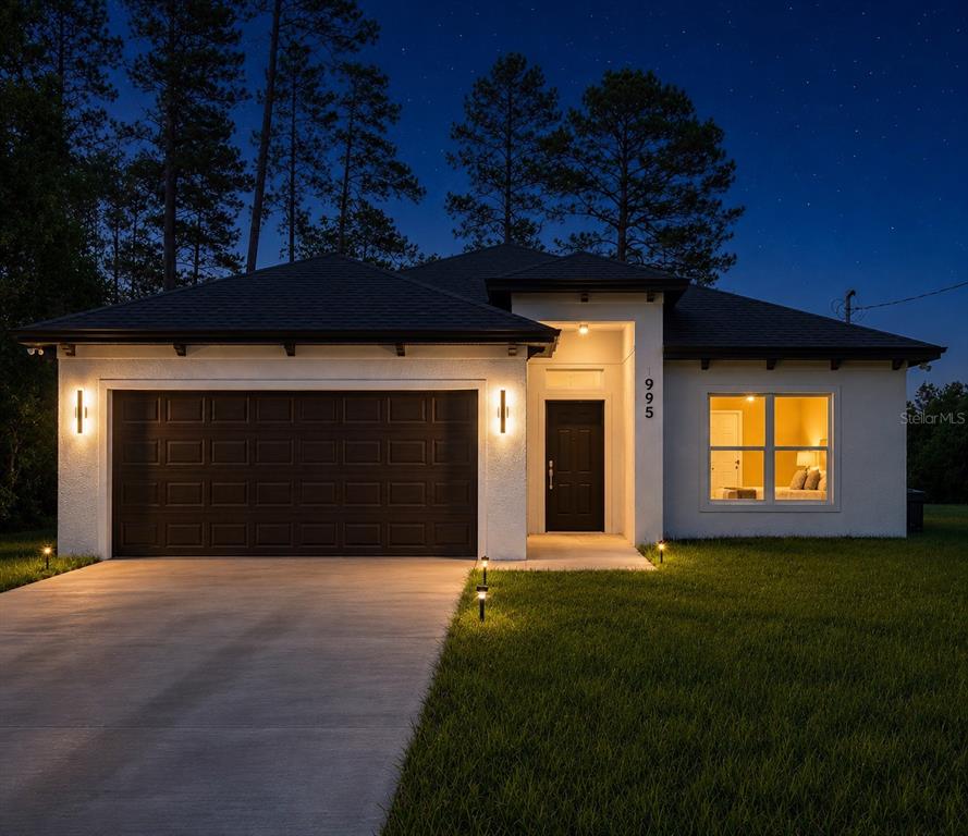 A single-story house with a dark garage door, white stucco walls, and a lit entryway — 995 9TH AVENUE, DELAND, FL