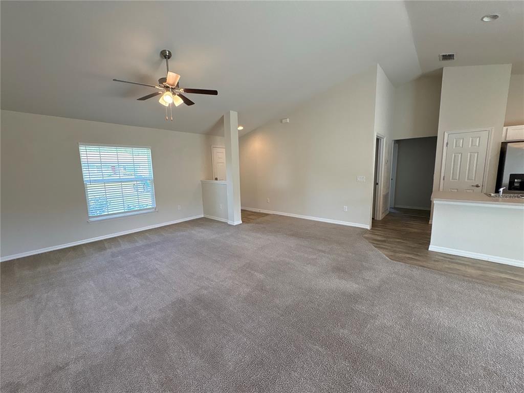A carpeted living room features a vaulted ceiling, a ceiling fan, and a window — 15415 SW 34TH AVENUE, OCALA, FL