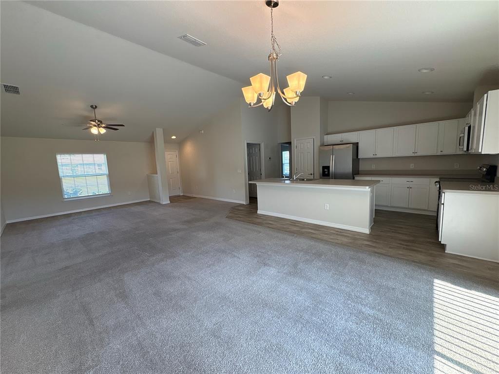 An open-concept living room and kitchen featuring gray carpeting, white cabinetry, and a center island — 15415 SW 34TH AVENUE, OCALA, FL