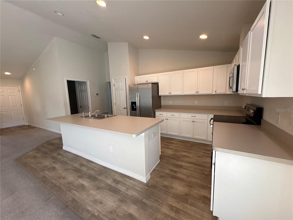 A kitchen features white cabinets, a central island, stainless steel appliances, and wood-look flooring — 15415 SW 34TH AVENUE, OCALA, FL
