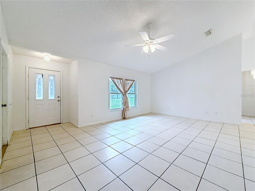 A bright, empty living room features white walls, light-colored floor tiles, and a ceiling fan — 4592 SW GARDENIA COURT, DUNNELLON, FL