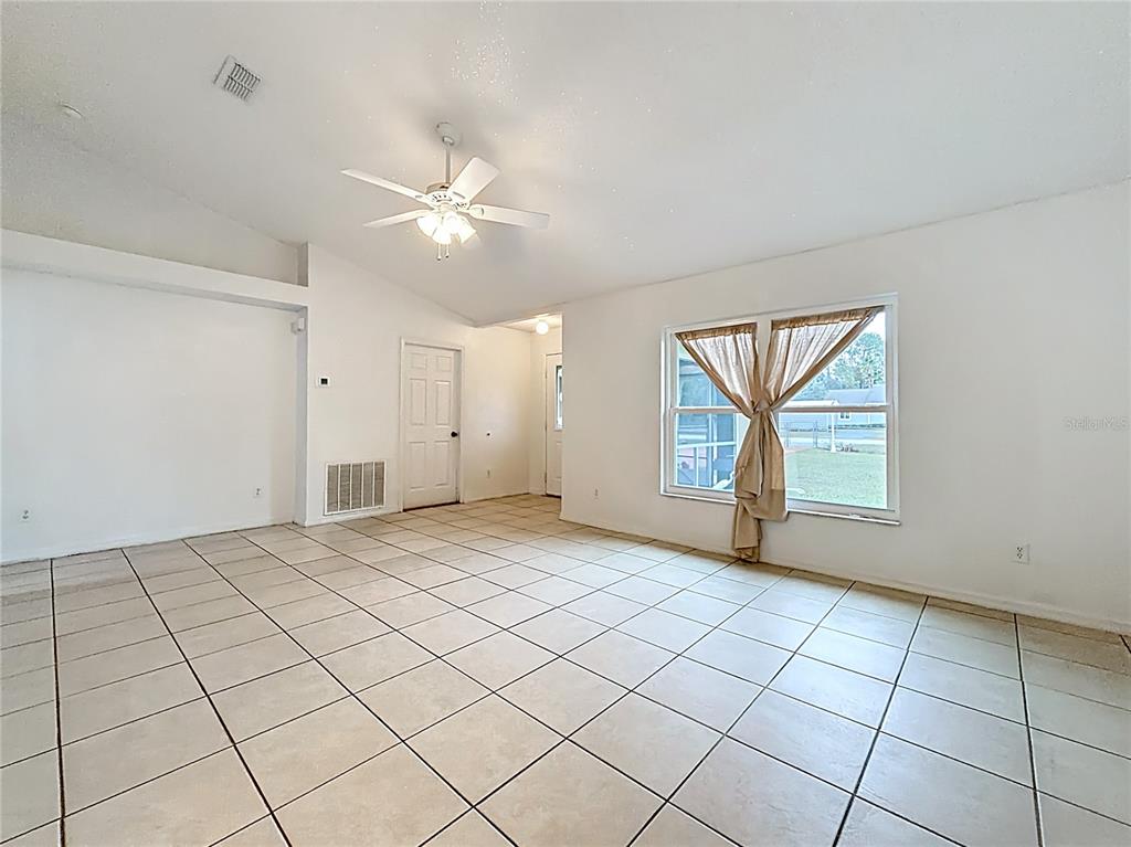 An empty room features white walls, light-colored tile flooring, a ceiling fan, and a window — 4592 SW GARDENIA COURT, DUNNELLON, FL