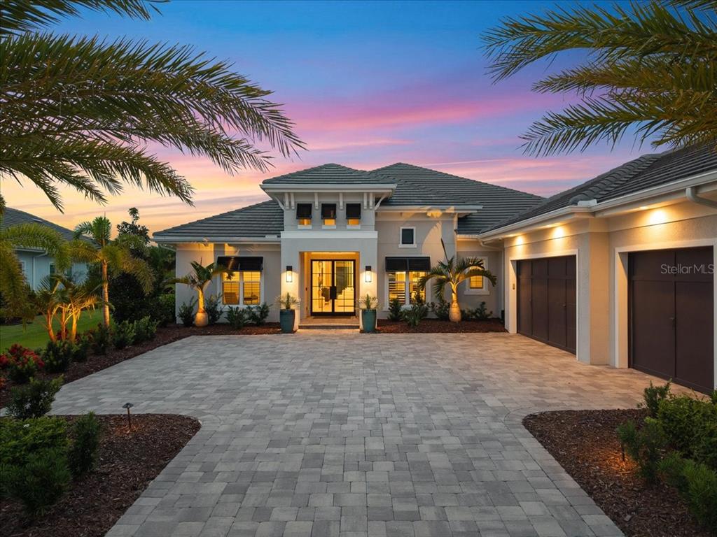 A modern single-story house with a paved driveway, palm trees, and a sunset sky — 7908 BOWSPIRIT WAY, LAKEWOOD RANCH, FL
