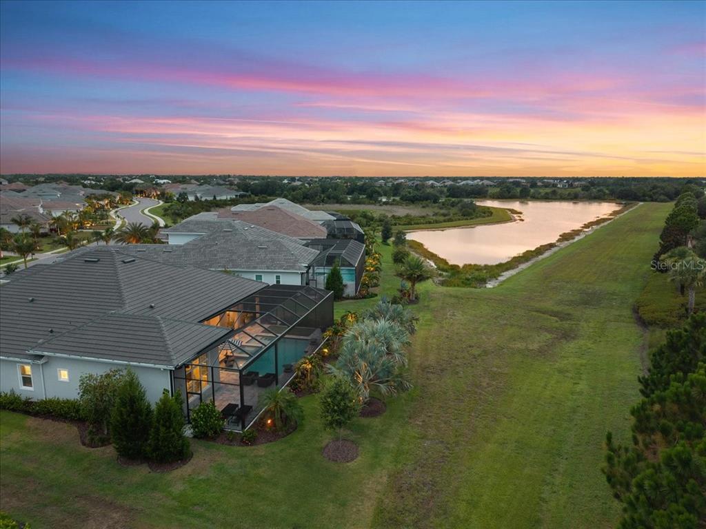 An aerial view shows a house with a screened-in pool overlooking a pond at sunset — 7908 BOWSPIRIT WAY, LAKEWOOD RANCH, FL