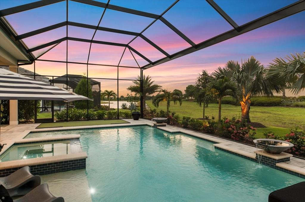 A screened-in pool patio features a spa, water bowls, and a view of a lake — 7908 BOWSPIRIT WAY, LAKEWOOD RANCH, FL