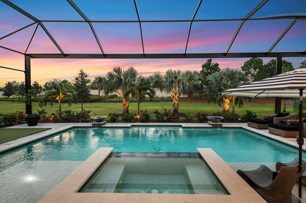 A screened-in pool and spa area overlooks a grassy backyard at sunset — 7908 BOWSPIRIT WAY, LAKEWOOD RANCH, FL