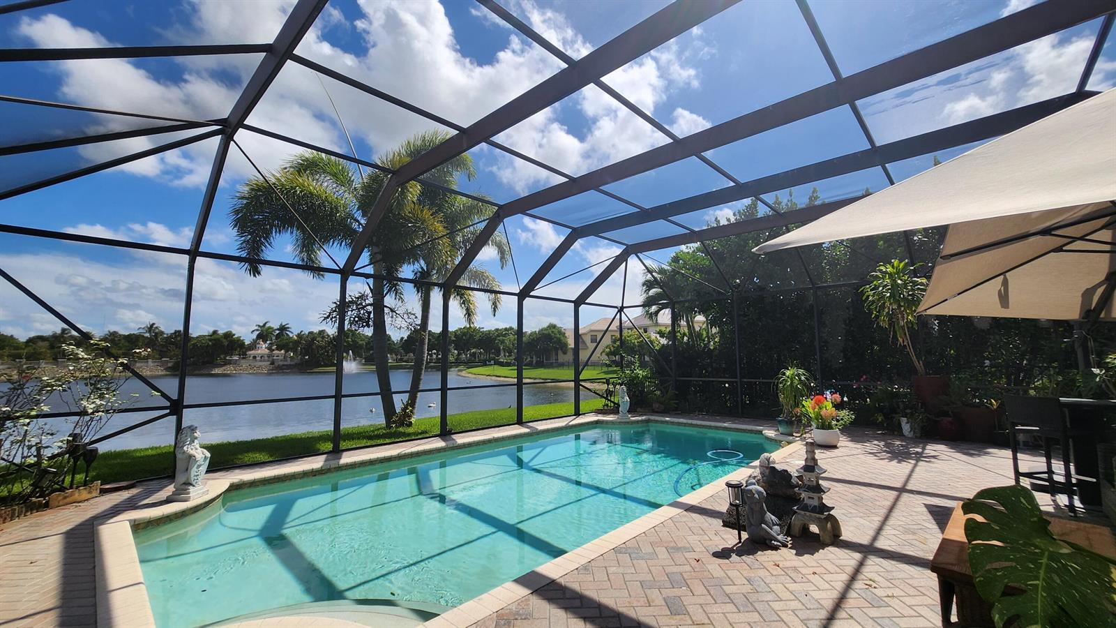 A screened-in pool patio overlooks a lake at sunset with palm trees in the background — 10334 Medicis Place, Wellington FL 33449, WELLINGTON, FL