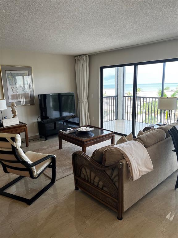 A living room features tile floors, a rattan sofa, and a balcony overlooking the ocean — 1102 BEN FRANKLIN DRIVE UNIT 514, SARASOTA, FL