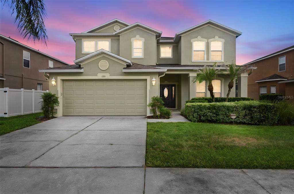 A two-story suburban house with a beige exterior, a two-car garage, and a front lawn — 125 NORFOLK DRIVE, DAVENPORT, FL