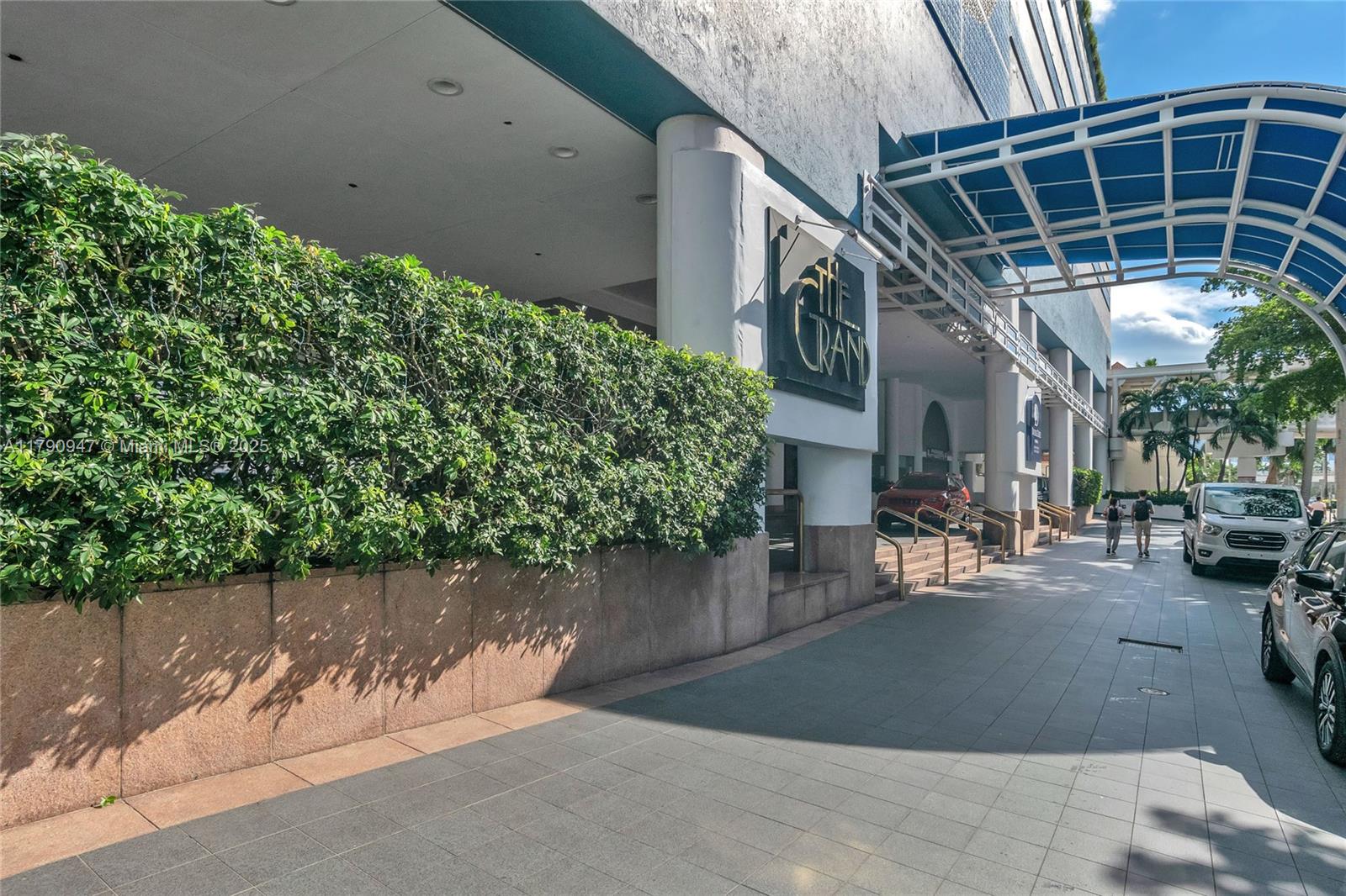 The exterior entrance of a building features a large hedge, a covered walkway, and signage — 1717 N Bayshore Dr # 3144, Miami FL 33132, MIAMI, FL