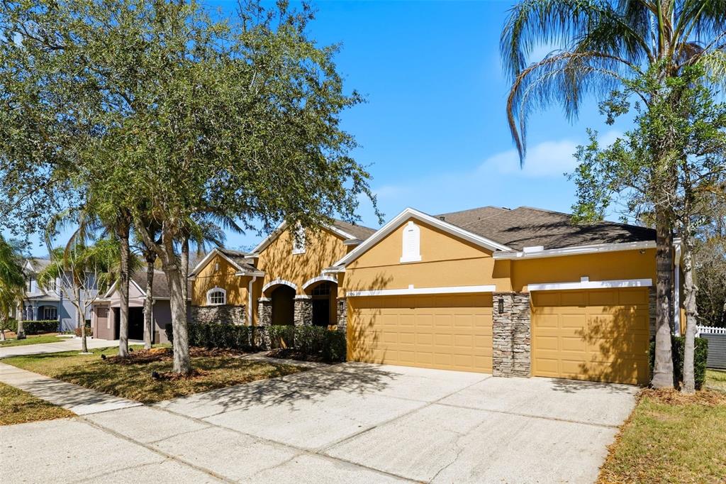 A single-story house with a three-car garage, stone accents, and mature trees in the yard — 1356 ANNA CATHERINE DRIVE, ORLANDO, FL