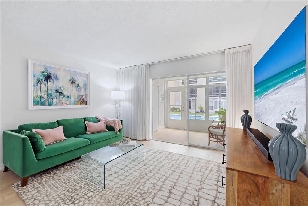 A living room features a green sofa, glass coffee table, and a large wall-mounted television — 995 LAGUNA DRIVE UNIT 103, VENICE, FL