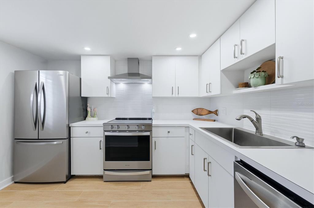 A modern kitchen features white cabinets, stainless steel appliances, and light wood-look flooring — 995 LAGUNA DRIVE UNIT 103, VENICE, FL