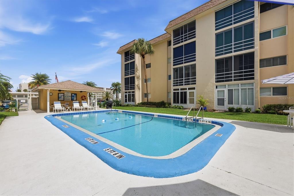 A swimming pool sits in front of a multi-story apartment building with a covered patio — 995 LAGUNA DRIVE UNIT 103, VENICE, FL