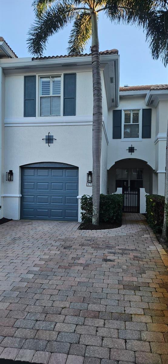 A two-story stucco townhouse features a blue garage door, a palm tree, and brick pavers — 179 Las Brisas Circle, Hypoluxo FL 33462, HYPOLUXO, FL