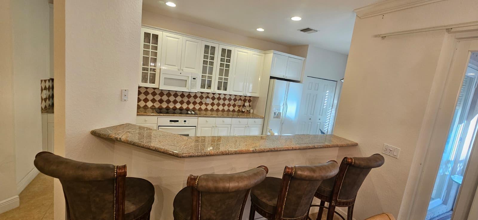 A kitchen features white cabinets, granite countertops, a tiled backsplash, and a breakfast bar — 179 Las Brisas Circle, Hypoluxo FL 33462, HYPOLUXO, FL