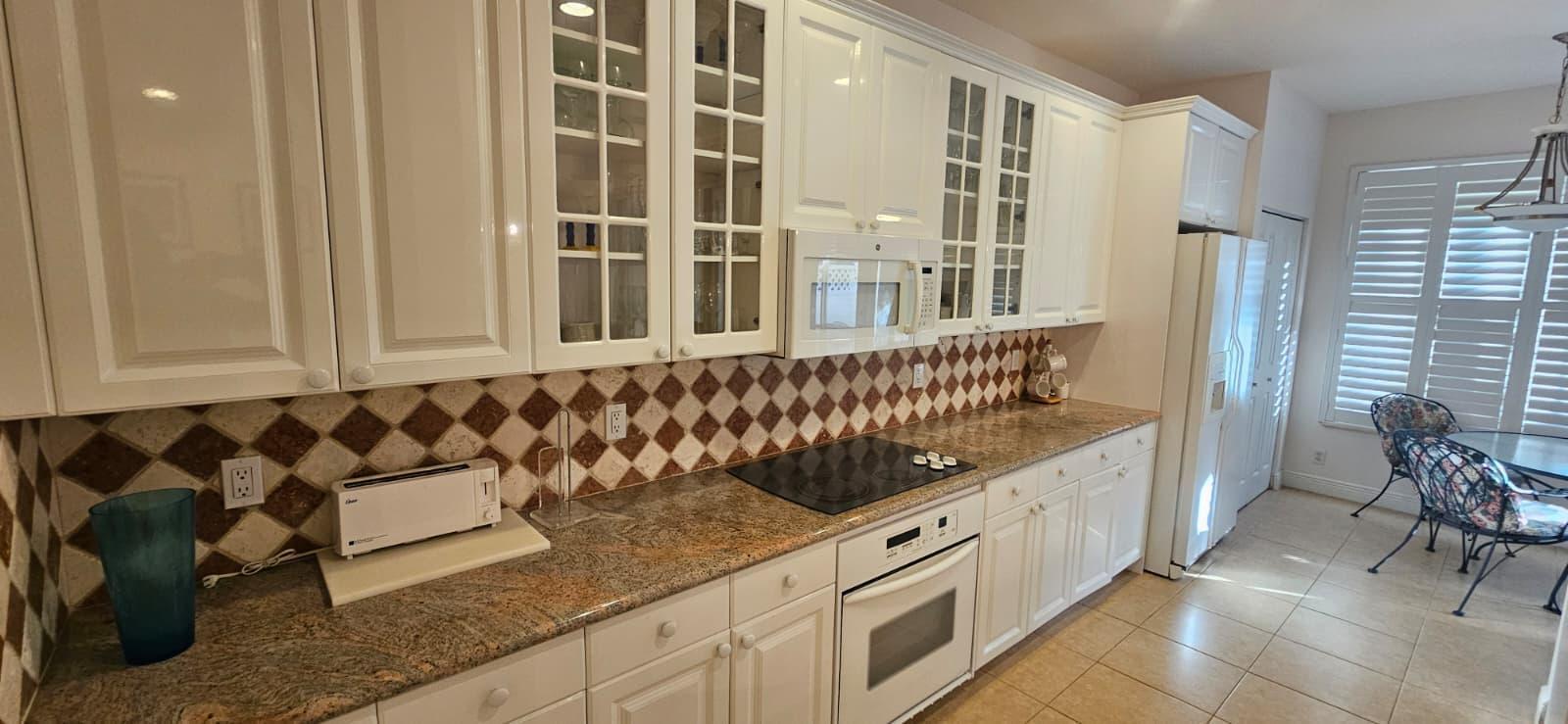 A kitchen with white cabinets, granite countertops, a diamond-patterned backsplash, and stainless steel appliances — 179 Las Brisas Circle, Hypoluxo FL 33462, HYPOLUXO, FL