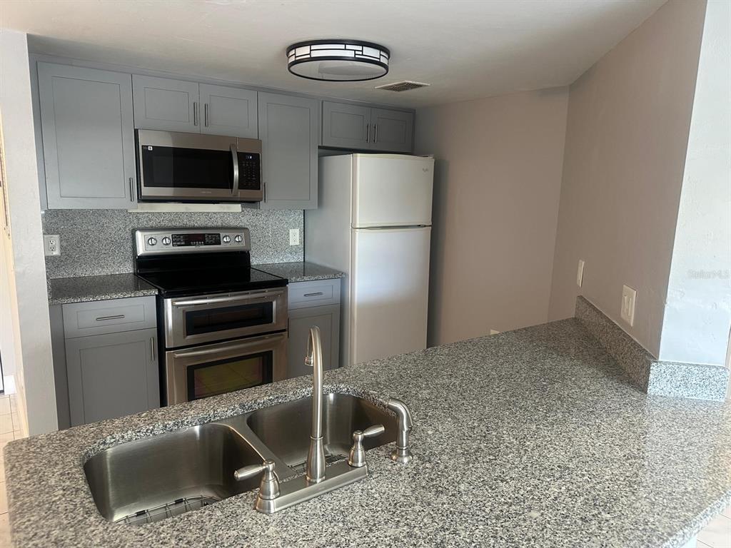 A kitchen features gray cabinets, granite countertops, stainless steel appliances, and a double-basin sink — 1767 FOUR MILE COVE PARKWAY UNIT 810, CAPE CORAL, FL