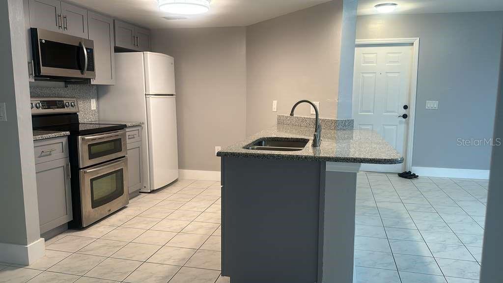 A kitchen features gray cabinets, stainless steel appliances, a granite-topped island, and white tile flooring — 1767 FOUR MILE COVE PARKWAY UNIT 810, CAPE CORAL, FL