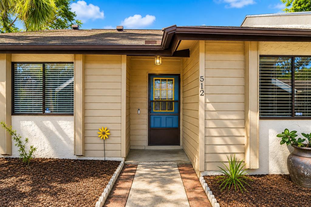 A tan house exterior features a blue front door, horizontal siding, and a concrete walkway — 512 DERBY DRIVE, ALTAMONTE SPRINGS, FL