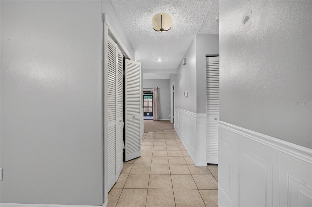 A hallway with tiled floors, white wainscoting, and louvered closet doors leads to another room — 512 DERBY DRIVE, ALTAMONTE SPRINGS, FL