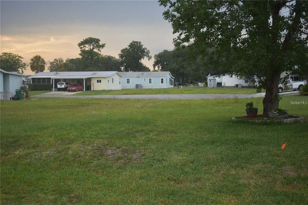A grassy lot faces a row of single-story mobile homes under a cloudy sky — LOT 18 BLK C CAMBRIDGE COURT, WILDWOOD, FL