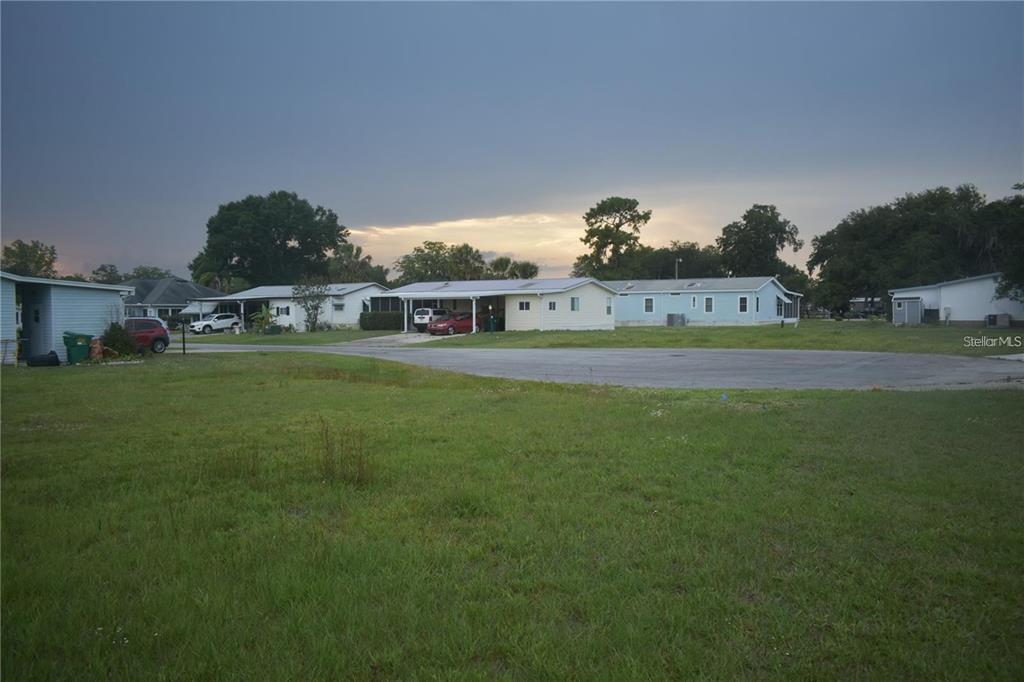 A grassy lot faces a row of single-story manufactured homes under a cloudy sky — LOT 18 BLK C CAMBRIDGE COURT, WILDWOOD, FL