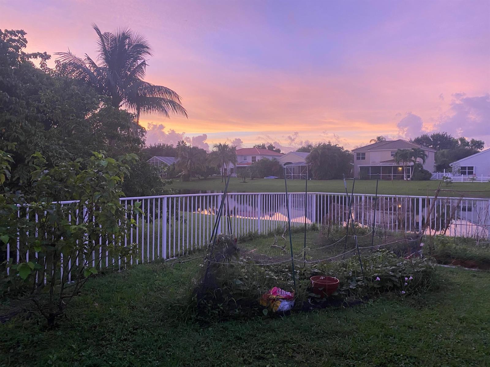 A backyard garden with a white fence overlooks a pond at sunset — 4080 Sea Grape Circle, Delray Beach FL 33445, DELRAY BEACH, FL