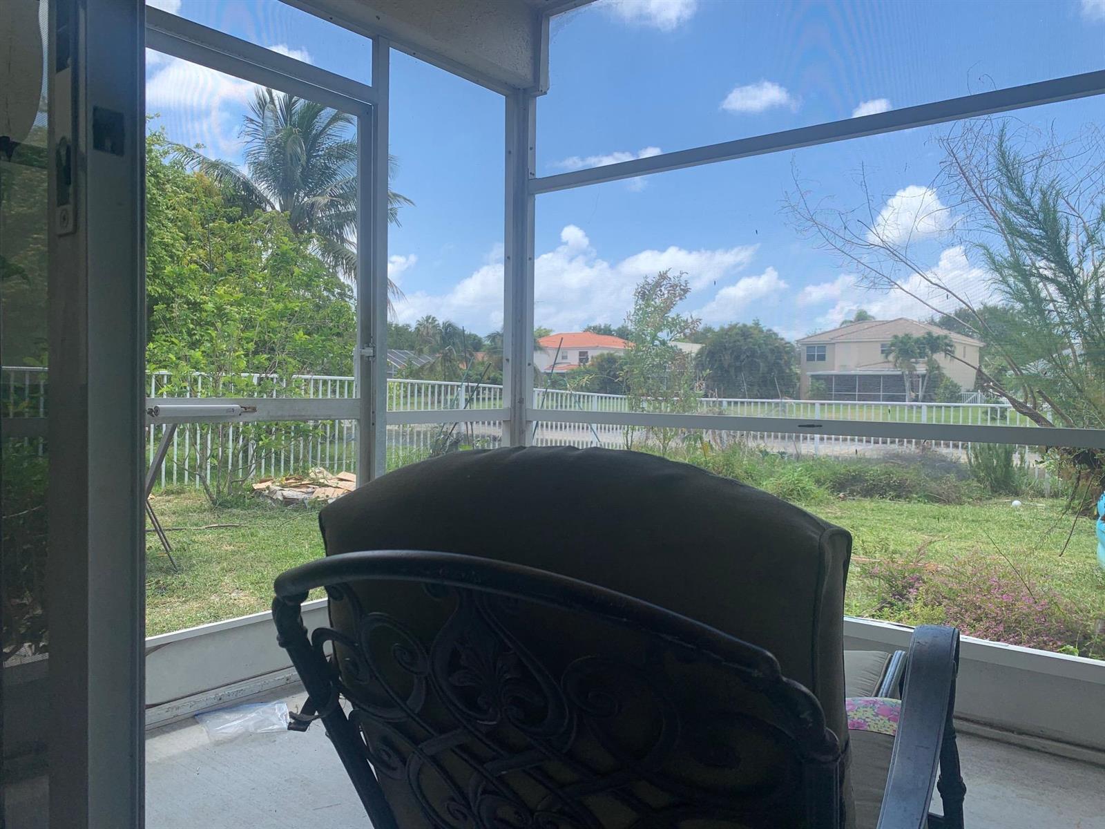 A view from a screened-in porch looking out at a backyard, fence, and neighboring houses — 4080 Sea Grape Circle, Delray Beach FL 33445, DELRAY BEACH, FL