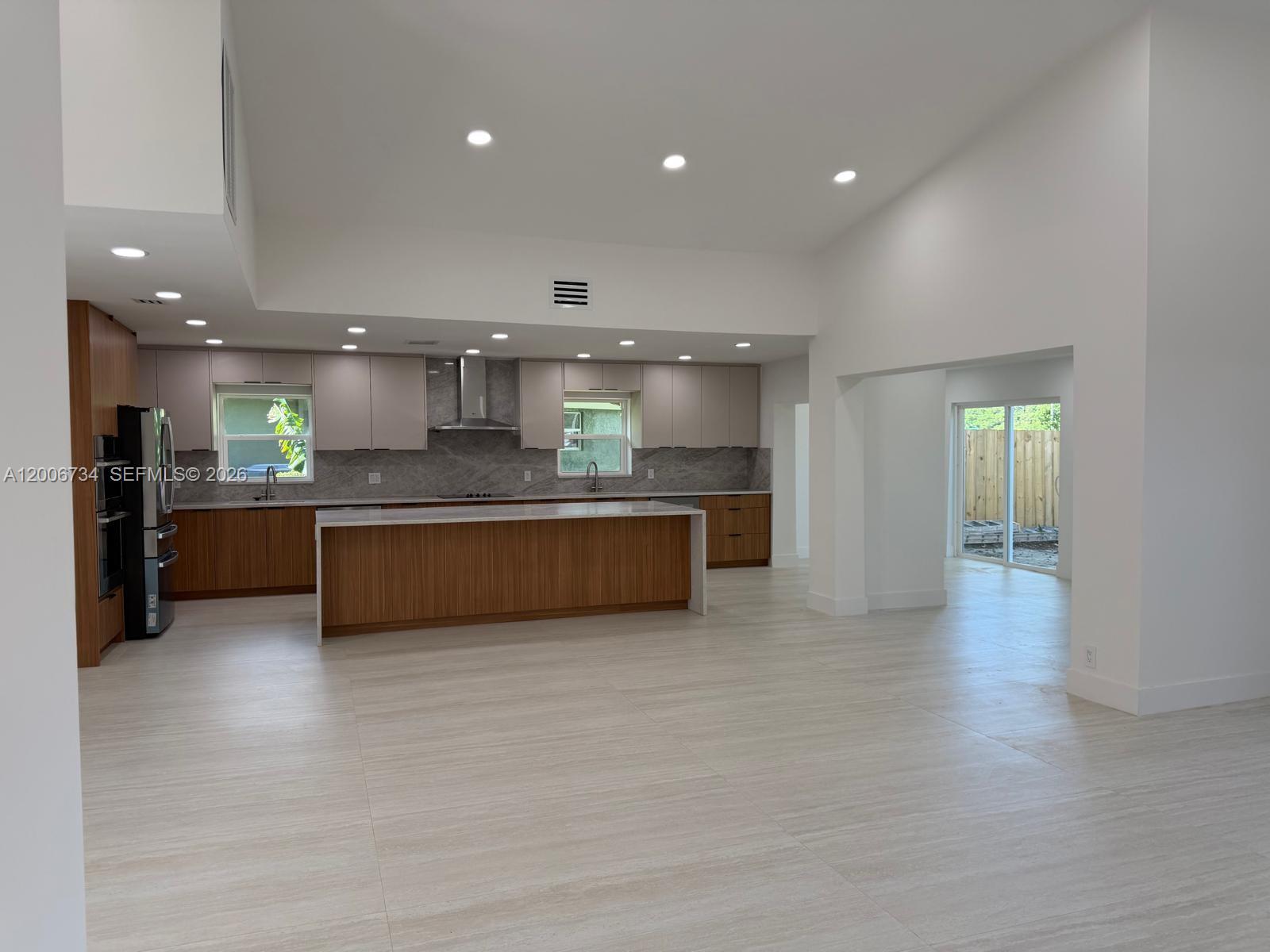 A modern kitchen features wood-toned cabinets, a large central island, and light-colored tile flooring — 7917 Chula Vista Cres, Boca Raton FL 33433, BOCA RATON, FL