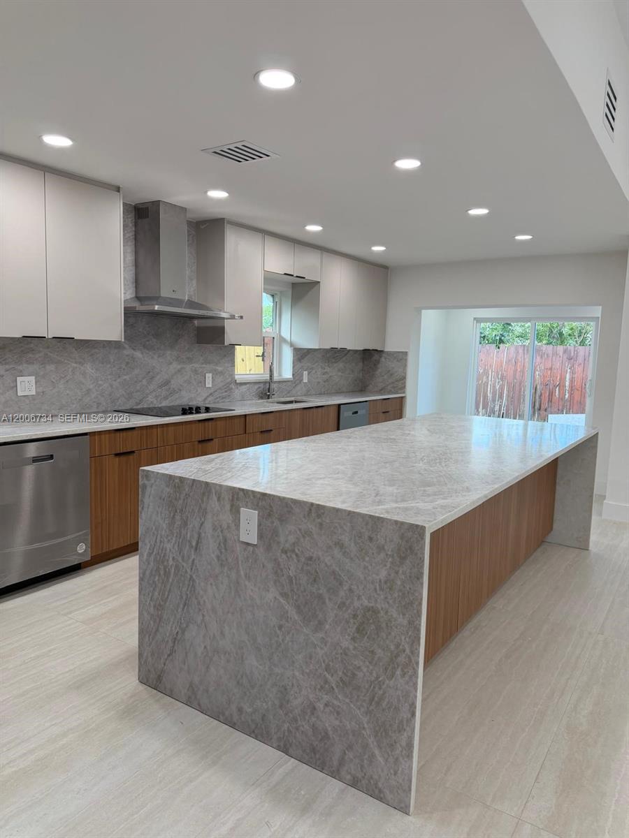 A modern kitchen features a large waterfall island, wood-toned cabinetry, and gray stone countertops — 7917 Chula Vista Cres, Boca Raton FL 33433, BOCA RATON, FL