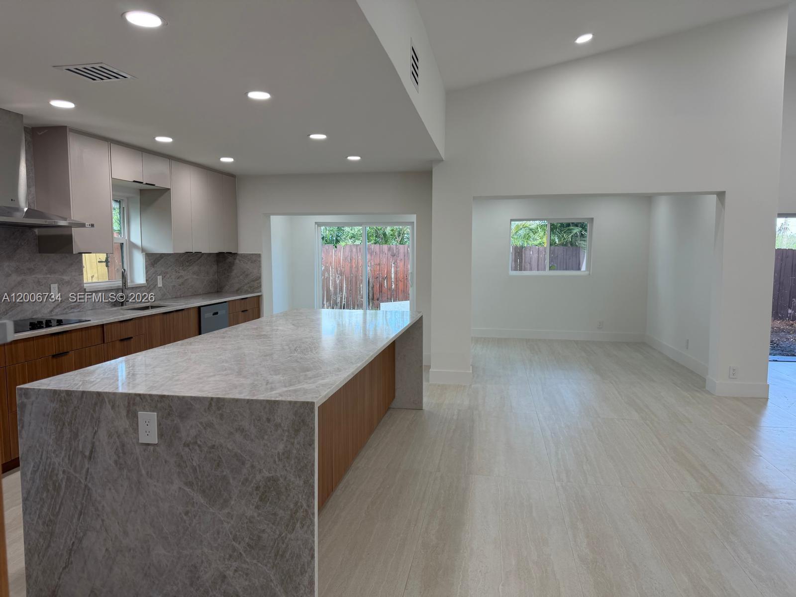 A modern kitchen features a large marble waterfall island, wood cabinetry, and light tile flooring — 7917 Chula Vista Cres, Boca Raton FL 33433, BOCA RATON, FL