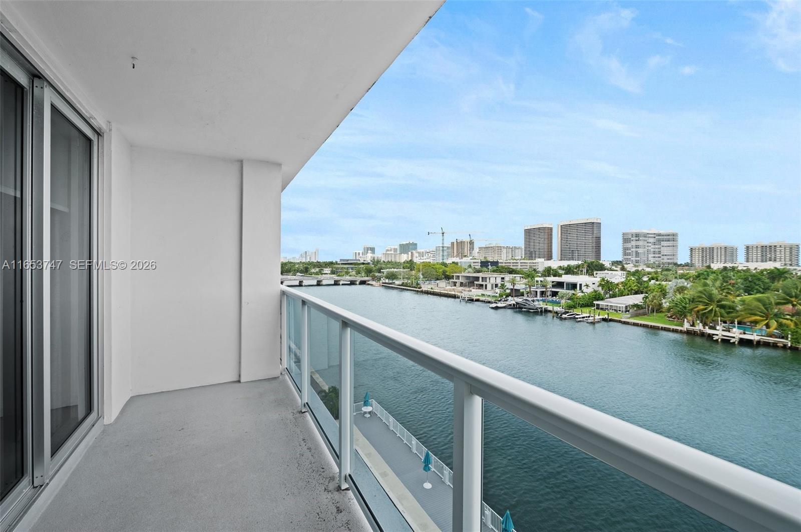 A balcony with a glass railing overlooks a canal and a city skyline — 9381 E Bay Harbor Dr # 603S, Bay Harbor Islands FL 33154, BAY HARBOR ISLANDS, FL