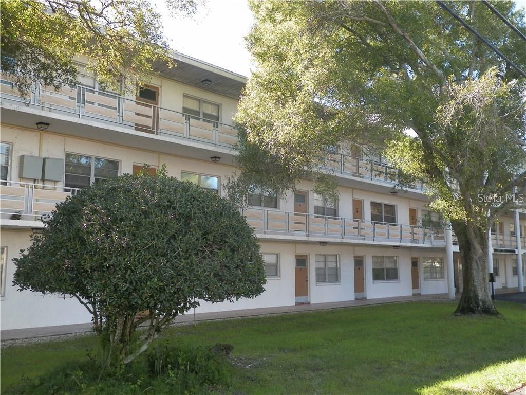 A three-story apartment building with exterior walkways and balconies sits behind a large tree — 911 WASHINGTON AVENUE UNIT 304, LARGO, FL