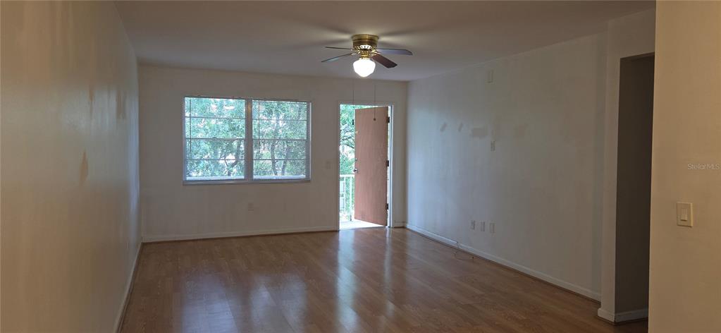 An empty living room features light wood flooring, white walls, a ceiling fan, and a balcony — 911 WASHINGTON AVENUE UNIT 304, LARGO, FL