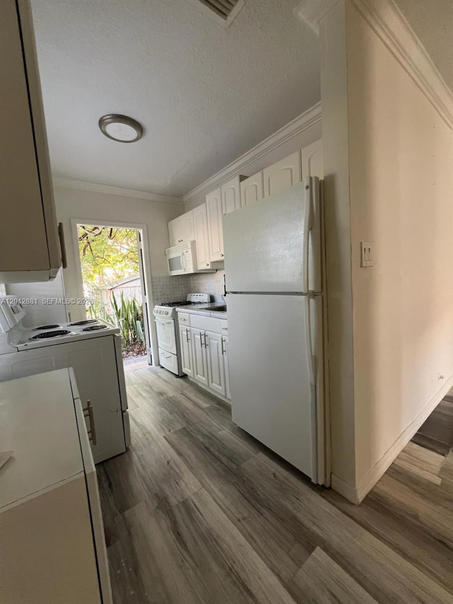 A kitchen features white cabinets, white appliances, and wood-look flooring leading to an exterior door — 915 N 19th Ave, Hollywood FL 33020, HOLLYWOOD, FL