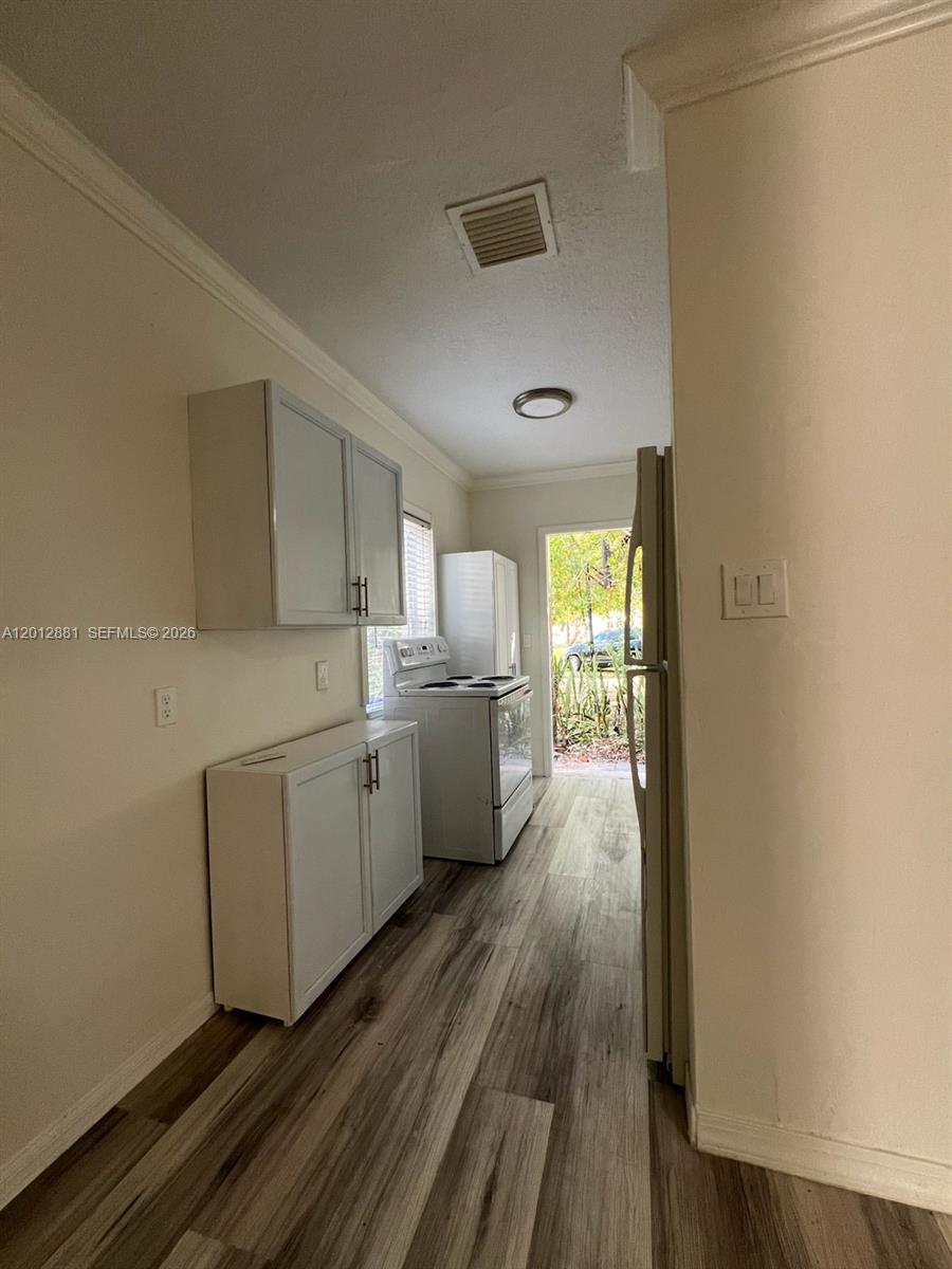 A narrow kitchen features white cabinets, stainless steel appliances, and wood-look flooring — 915 N 19th Ave, Hollywood FL 33020, HOLLYWOOD, FL