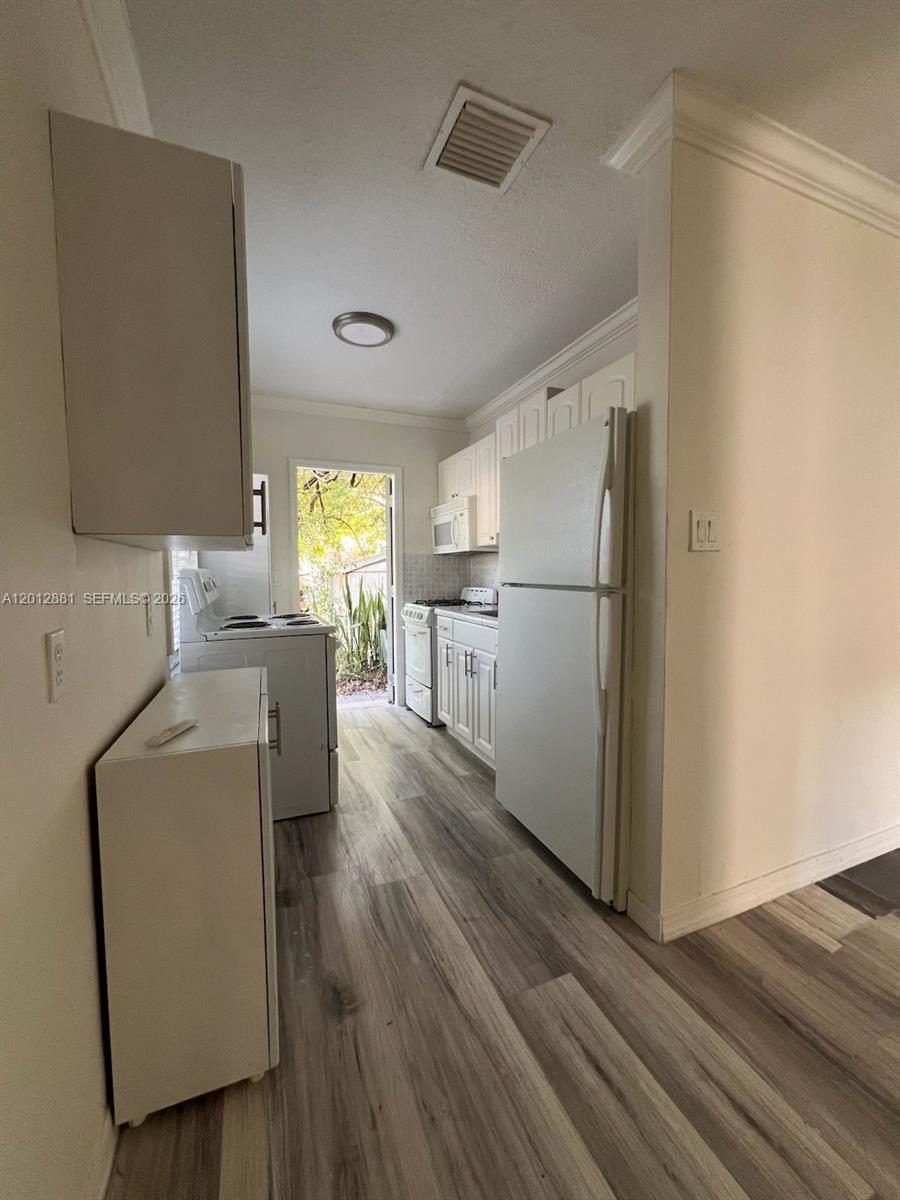 A galley-style kitchen features white cabinetry, white appliances, and light wood-look flooring — 915 N 19th Ave, Hollywood FL 33020, HOLLYWOOD, FL