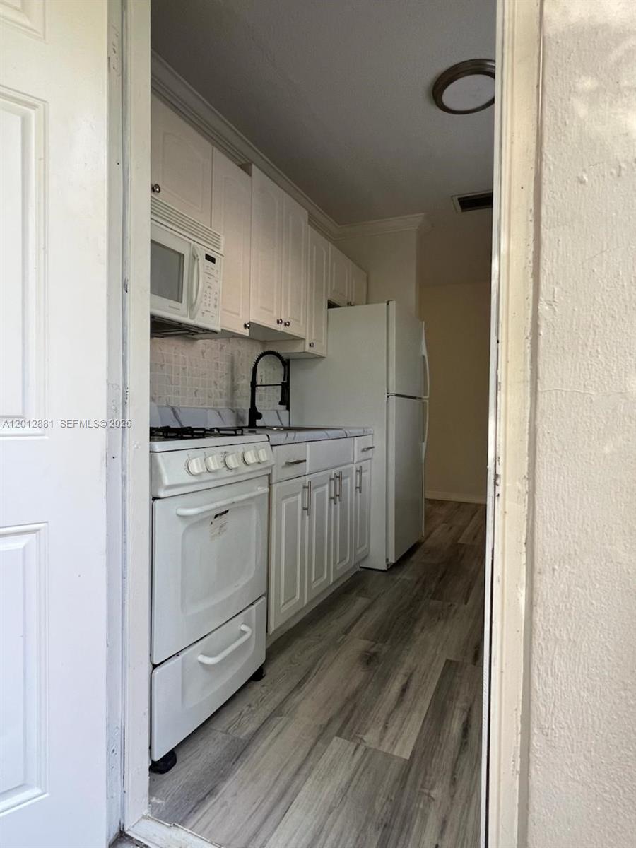 A narrow galley kitchen features white cabinets, white appliances, and wood-look flooring — 915 N 19th Ave, Hollywood FL 33020, HOLLYWOOD, FL