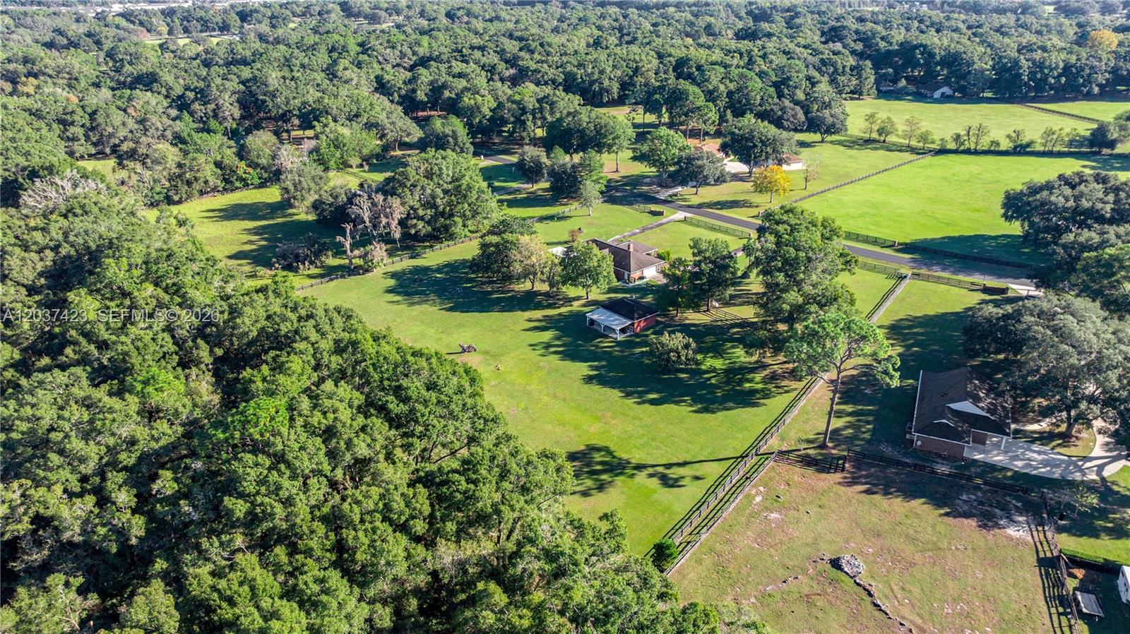 An aerial view shows a rural property with multiple houses, fenced pastures, and dense trees — OCALA, FL