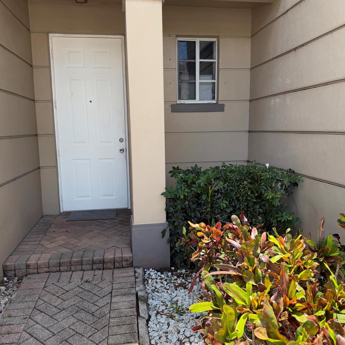 A white front door is adjacent to a small window and a landscaped garden bed — 976 Abaco Lane, West Palm Beach FL 33404, WEST PALM BEACH, FL