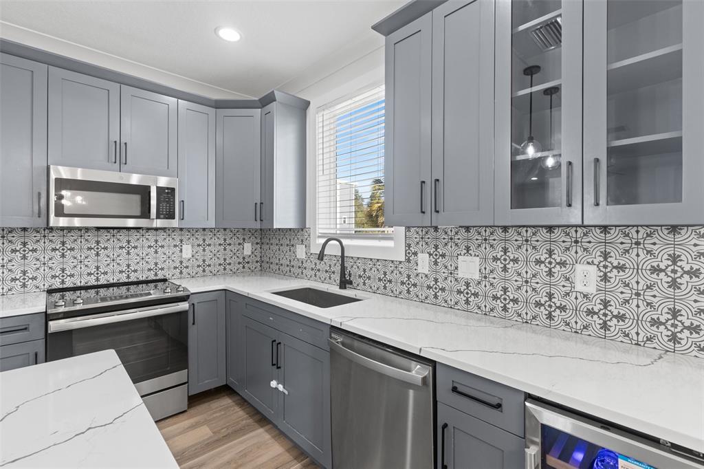 A kitchen features gray cabinets, patterned tile backsplash, white countertops, and stainless steel appliances — 1501 N MORGAN STREET UNIT 5, TAMPA, FL