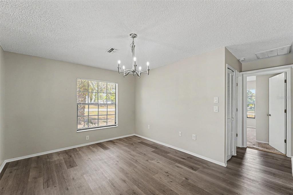 An empty dining room features a chandelier, a window with blinds, and wood-look flooring — 10161 HEATHCLIFF STREET, SPRING HILL, FL