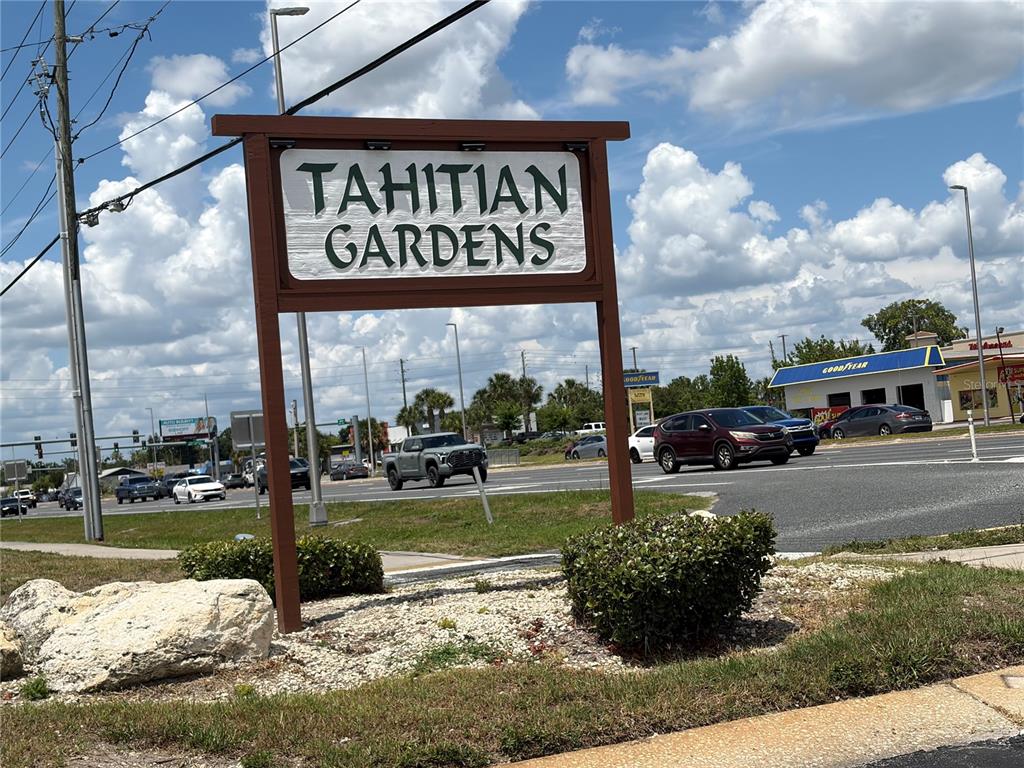 A wooden sign for Tahitian Gardens stands in a landscaped area near a busy road — 4345 TAHITIAN GARDENS CIRCLE UNIT C, HOLIDAY, FL