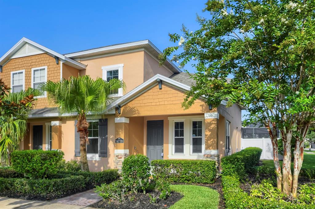 A two-story stucco townhouse with a front porch, tan siding, and a landscaped yard — 14778 PEEKSKILL DRIVE, WINTER GARDEN, FL