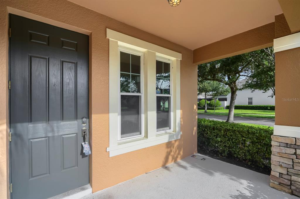 A covered front porch features a dark gray door, two windows, and stone pillar accents — 14778 PEEKSKILL DRIVE, WINTER GARDEN, FL