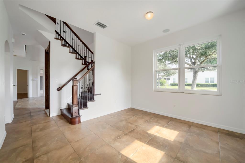 An empty room features large square floor tiles, white walls, and a wooden staircase — 14778 PEEKSKILL DRIVE, WINTER GARDEN, FL